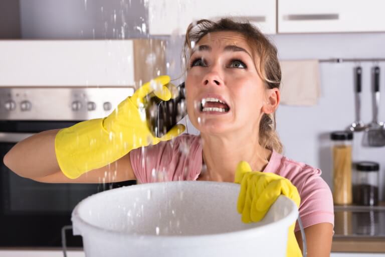 A woman tries to prevent water damage by holding a bucket to catch water from the ceiling.