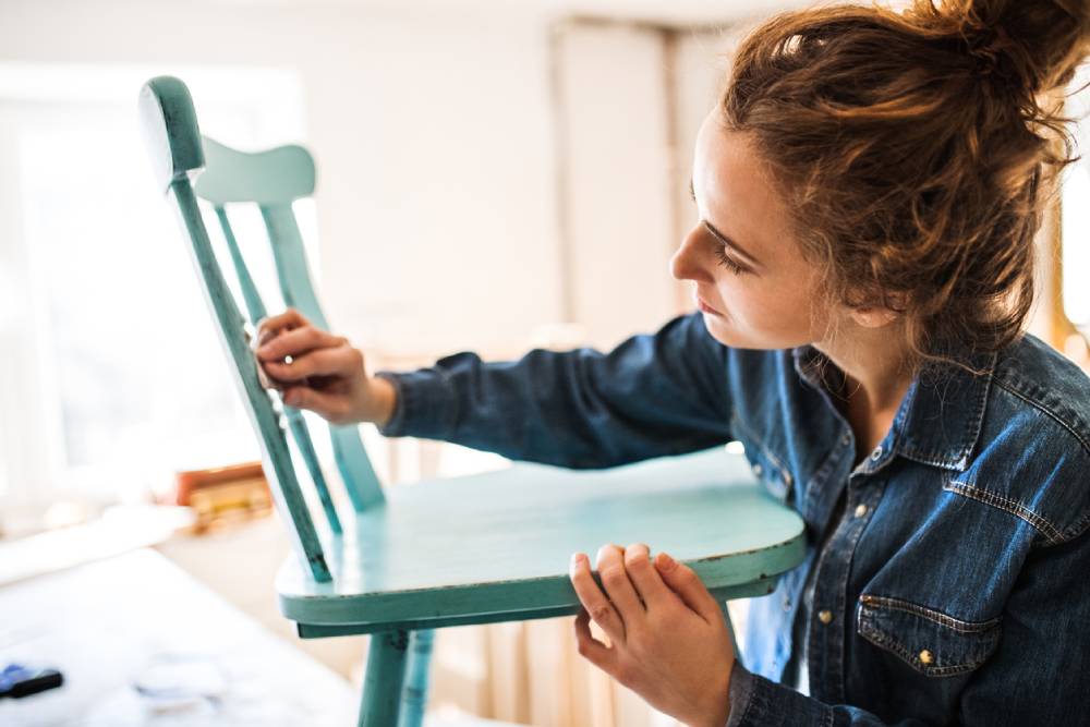 Woman sanding down a wooden chair for her restoration project